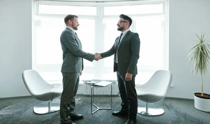 Two young successful businessmen in suits shaking hands after negotiation
