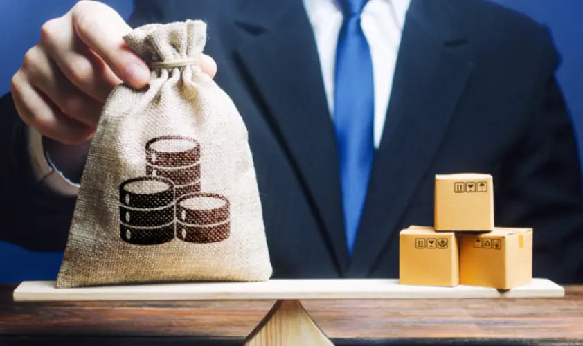 Businessman puts a money bag and bunch of boxes on scales