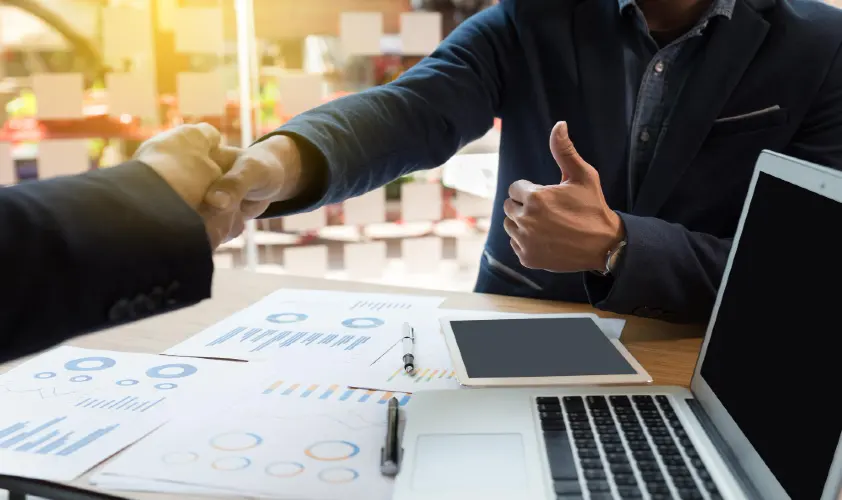 Midsection of man using laptop and shaking hands while charts on table